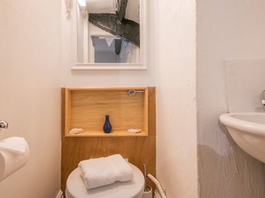 A small bathroom with a toilet towel and sink with a mirror and wooden shelf with decorative items at Cloam Cottage in Port Isaac