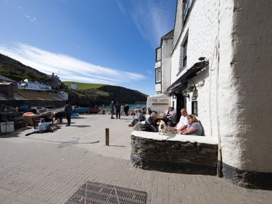 People sitting outside a bar and restaurant near a waterfront with boats and hills in the background at Cloam Cottage Port Isaac