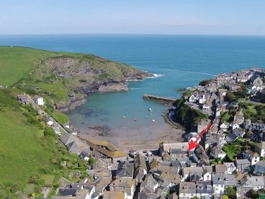 An aerial view of a coastal village with houses near a small harbor and green hills at Cloam Cottage in Port Isaac