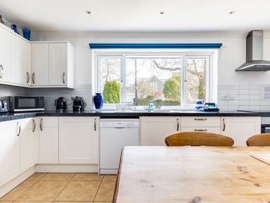 A kitchen with white cabinets a dishwasher a wooden table and chairs and a window showing trees outside at Rock Hill in Rock