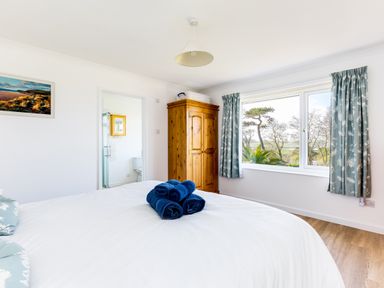 A bedroom with a bed with blue towels on top a wooden wardrobe a window with curtains and a door leading to a bathroom at Rock Hill in Rock