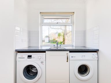 A laundry room with a washing machine and dryer under a countertop with a sink and window at Rock Hill in Rock