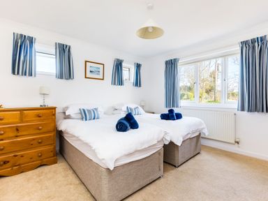 A bedroom with two single beds side by side with white bedding and blue towels on top with a wooden dresser and blue striped curtains at Rock Hill in Rock