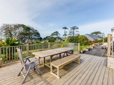 An outdoor wooden deck with a table, bench, and chairs overlooking a garden with trees at Rock Hill in Rock