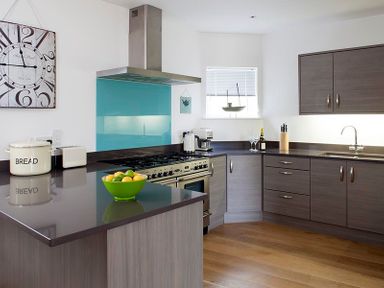 A kitchen with gray cabinets a countertop stove a green bowl of fruit and a sink at The Beach Hut in Polzeath