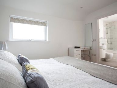 A bedroom with a bed and pillows a desk with a chair and a door leading to a bathroom at The Beach Hut in Polzeath