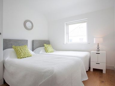 A bedroom with two single beds a window and a bedside table with lamp at The Beach Hut in Polzeath