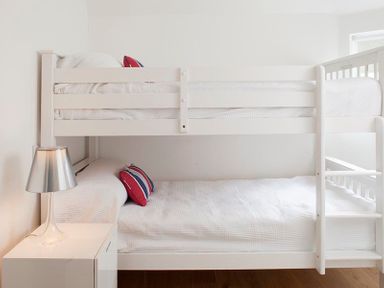 A bedroom with white bunk beds and a bedside table with a lamp at The Beach Hut in Polzeath