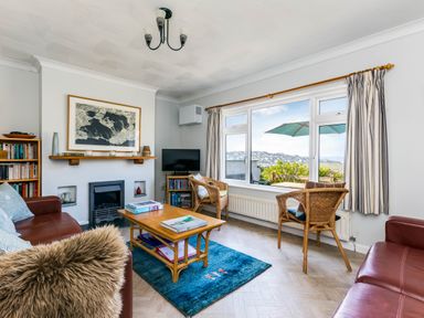 A living room with red leather sofas a wooden coffee table a blue rug and a window showing an outdoor view at Bella Vista in Polzeath