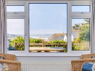 A view through three pane windows showing a wooden picnic table outside and houses with greenery in the background at Bella Vista in Polzeath