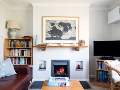 A living room with a fireplace a bookshelf a TV and a coffee table with books at Bella Vista in Polzeath