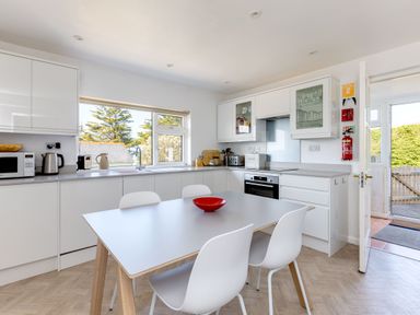 A kitchen with a dining table and chairs a stove and a window at Bella Vista in Polzeath