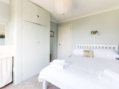 A bedroom with a double bed white linens wall-mounted light and built-in wardrobe at Bella Vista in Polzeath