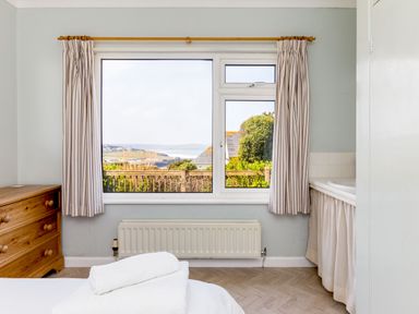 A bedroom with a wooden chest of drawers a radiator a window with striped curtains and a bed with folded towels at Bella Vista Polzeath