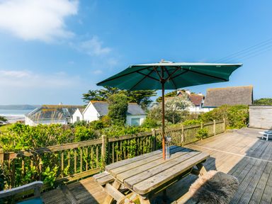 An outdoor wooden deck with a picnic table and large umbrella overlooking houses and greenery at Bella Vista in Polzeath
