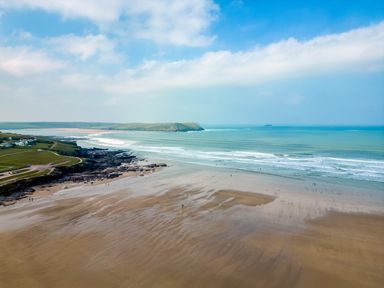 A sandy beach with waves and rocky areas near green hills and houses at Bella Vista in Polzeath