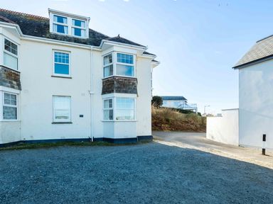 Exterior view of a white two-story building with several windows and a gravel driveway at Pinewood Flat 5 in Polzeath