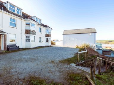 An outdoor space with white buildings a gravel area and wooden stairs leading down at Pinewood Flat 5 in Polzeath