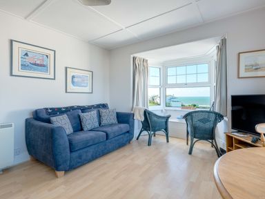 A living room with a blue sofa and two chairs by a window with ocean view at Pinewood Flat 5 in Polzeath