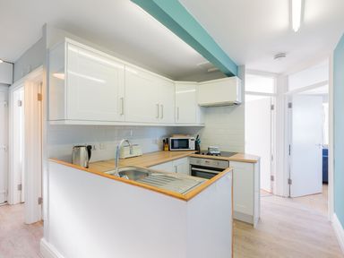 A kitchen with white cabinets wooden countertops and a stainless steel sink at Pinewood Flat 5 Polzeath