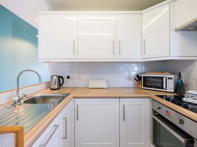 A kitchen with white cabinets a sink kettle toaster microwave and oven at Pinewood Flat 5 Polzeath