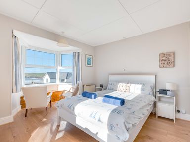 A bedroom with a double bed two blue towels on the bed two chairs by the window with seaside view at Pinewood Flat 5 in Polzeath