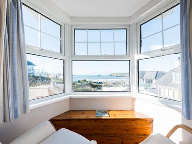 A bay window with a wooden bench and two chairs looking out at a coastal view at Pinewood Flat 5 in Polzeath