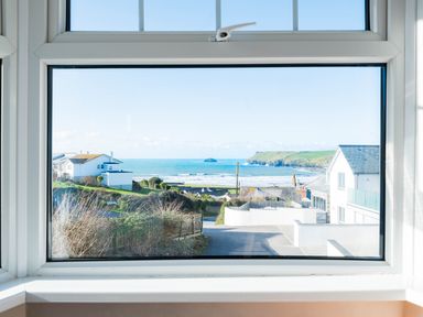 A coastal view with houses and a beach seen through a window at Pinewood Flat 5 in Polzeath
