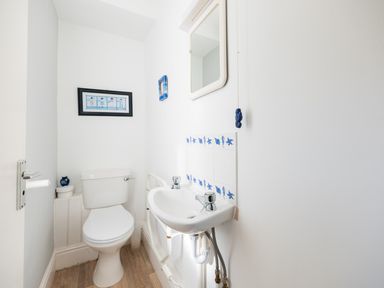 A small bathroom with a toilet and a wall-mounted sink with blue decorative tiles and two framed pictures at Pinewood Flat 5 Polzeath