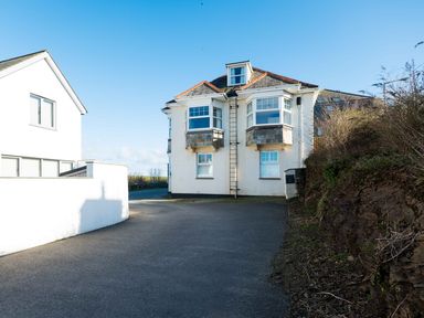 A paved driveway leading to the back of a two-story house with a dormer window and bay windows at Pinewood Flat 5 in Polzeath