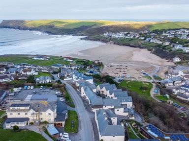 A coastal village with houses roads a sandy beach and green cliffs at Pinewood Flat 5 in Polzeath