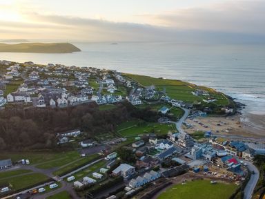 An aerial view of a coastal village with houses roads green fields and a beach at Pinewood Flat 5 Polzeath