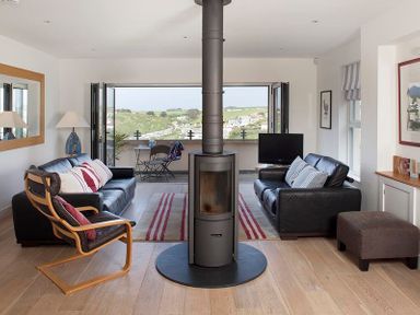 A living room with two black sofas a wood burning stove and a folding door leading to a balcony at Kellan in Polzeath