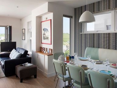A dining area with a table set with plates and glasses next to a living space with a sofa and television at Kellan in Polzeath