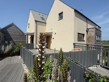 A decked area with plants and a gray fence outside modern beige houses at Kellan in Polzeath