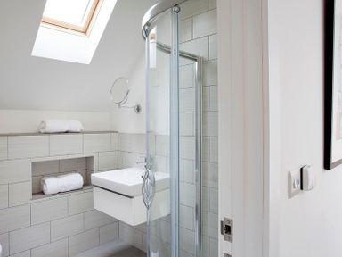 A bathroom with a walk in shower a wall mounted sink rolled towels and a skylight at Kellan in Polzeath