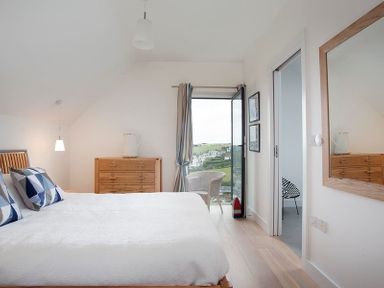 A bedroom with a bed pillows wooden dresser chair open door and a wall mirror at Kellan in Polzeath