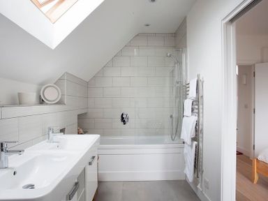 A bathroom with a double sink, bathtub with shower, towel rail and skylight at Kellan in Polzeath