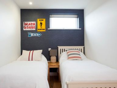 A bedroom with two single beds a nightstand with a lamp and wall signs at Kellan in Polzeath