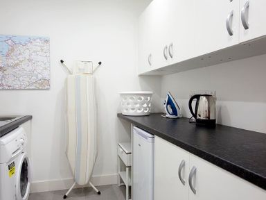 A laundry room with a washing machine ironing board laundry basket kettle and iron at Kellan Polzeath