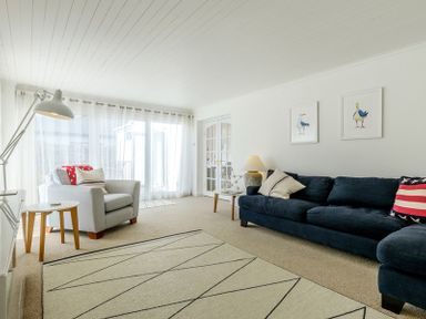 A living room with a blue sofa and armchair with pillows a floor lamp and framed bird pictures at The Moorings in Rock