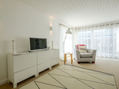 A living room with a white cabinet holding a television two candlesticks a chair with pillows a small round table and a floor lamp at The Moorings in Rock