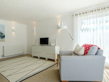 A living room with a striped armchair a floor lamp a white cabinet a television and a rug at The Moorings in Rock