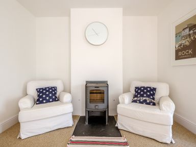 Two white armchairs with blue star patterned cushions on either side of a small stove with a clock above it at The Moorings in Rock