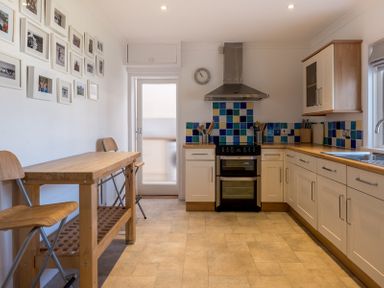 A kitchen with wooden dining table and two chairs a stove with a stainless steel hood and blue tiled backsplash at The Moorings in Rock