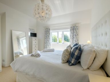 A bedroom with a bed with pillows and rolled towels a mirror a chest of drawers and windows with curtains at The Moorings in Rock