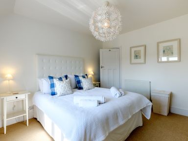 A bedroom with a double bed with blue and white pillows two bedside tables with lamps and rolled towels on bed at The Moorings in Rock
