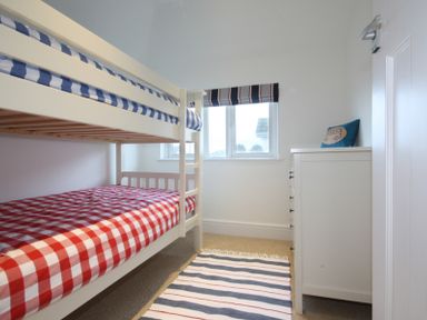 A small bedroom with white bunk beds and striped bedding a white dresser and a striped rug at The Moorings in Rock