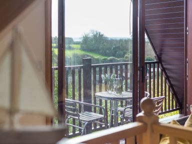A balcony with a round table set with a vase of flowers and wine glasses viewed through a glass door at Sandy Hills 8 in Rock