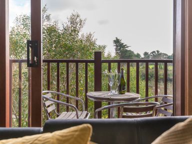 A balcony with a round wooden table two metal chairs and a bottle with glasses overlooking trees at Sandy Hills 8 Rock